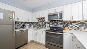 A modern kitchen with white cabinets, a stainless steel refrigerator, a microwave, a stove, and a dishwasher. - Emerald Skye 63 1 Bedroom Condo (Orange Beach)