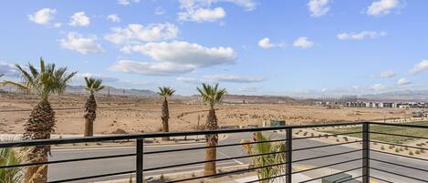 A balcony with a view of a desert landscape, palm trees, and distant mountains.