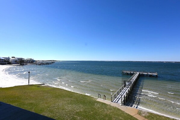 A coastal view with a pier extending into the water, a grassy area, and buildings in the background. - Sound Life 1 Bedroom Condo (Navarre)