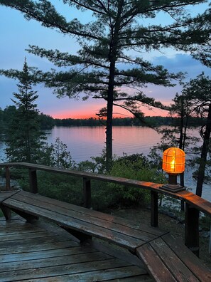 A wooden deck with a railing overlooking a lake at sunset. - Iconic Double A Frame Island Cottage in the Muskokas (Georgian Bay)