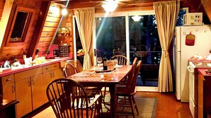 Una cocina acogedora con armarios de madera, una mesa de comedor y sillas. Hay un refrigerador y una ventana con cortinas.