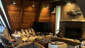 Un acogedor interior de cabaña de troncos con una televisión grande, muebles de mimbre y una chimenea.