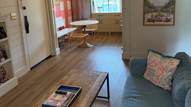 Una sala de estar moderna con un sofá, una mesa de centro y un comedor con mesa y sillas. Se ve una cocina al fondo.