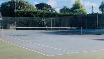 Een tennisbaan buiten met net, omringd door een hek en bomen.