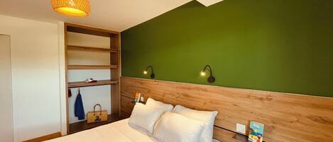 A bedroom with a bed, a wooden headboard, a green wall, and a hanging light fixture.