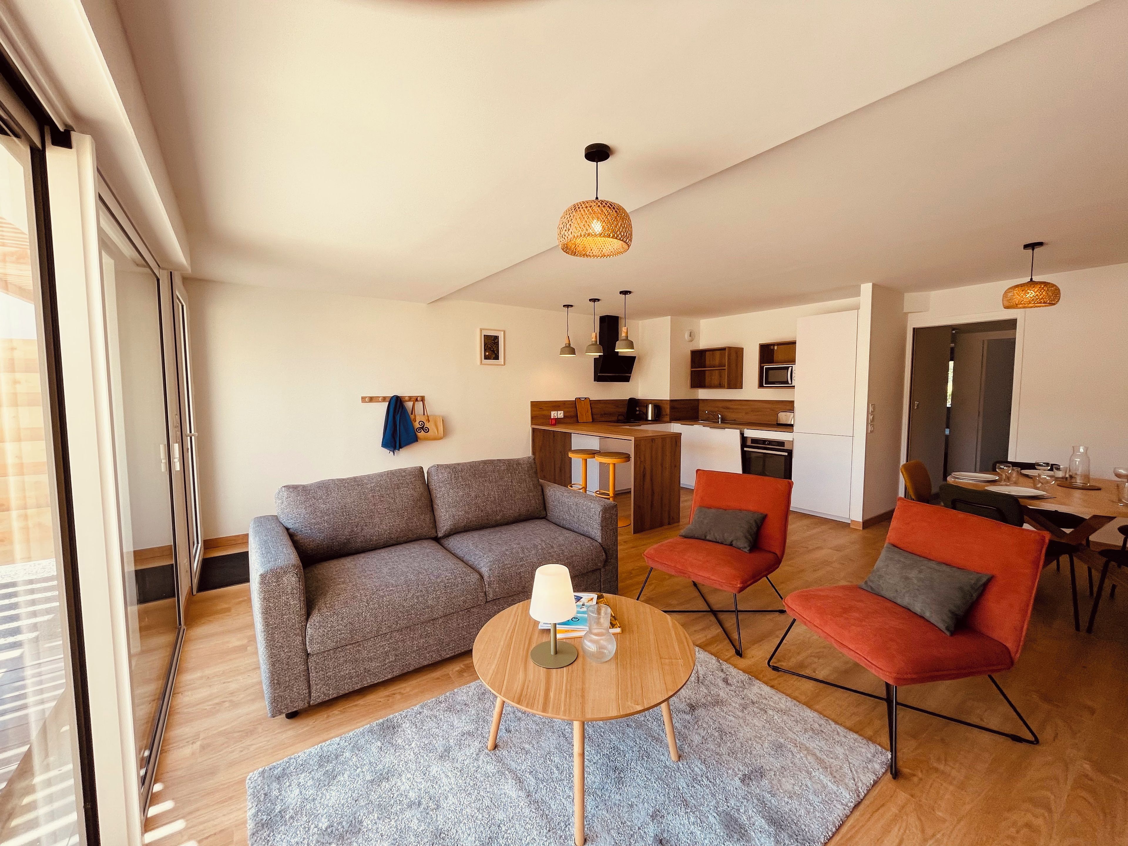 A modern living room with a sofa, two armchairs, a coffee table, and a dining area with a table and chairs.