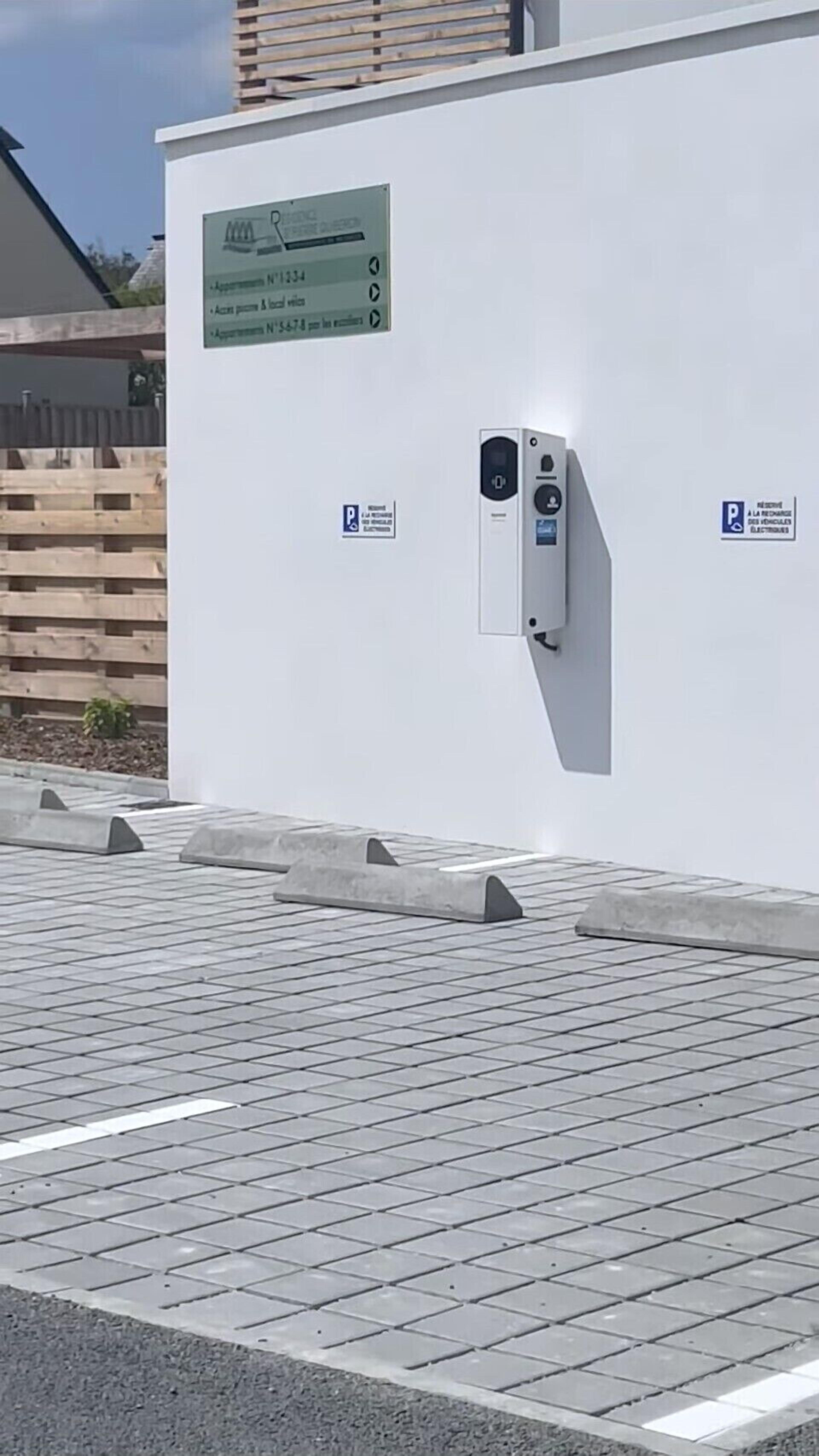 A parking area with electric vehicle charging stations, a sign indicating parking availability, and a white wall with a plaque.