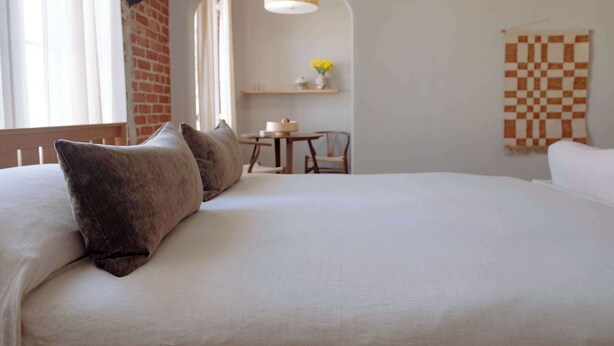 Een slaapkamer met een groot bed, een kleine tafel met stoelen, een hanglamp en een geruit wandtapijt.