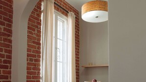 Een kamer met bakstenen muren, een houten vloer, een tafel met een schaal en een kaars, en een hangende lamp.