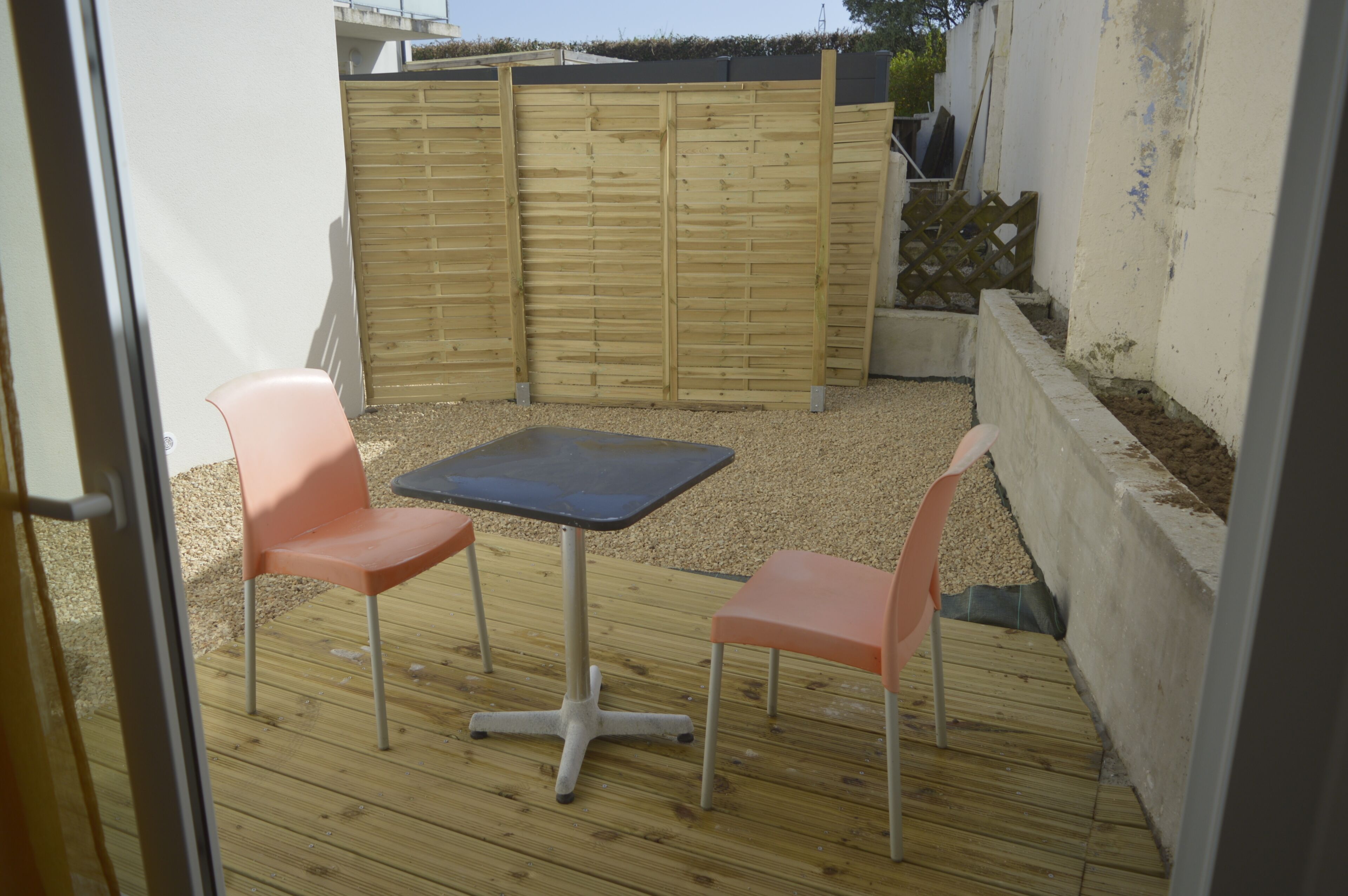 A patio area with a table and two chairs, a wooden fence, and a concrete planter.