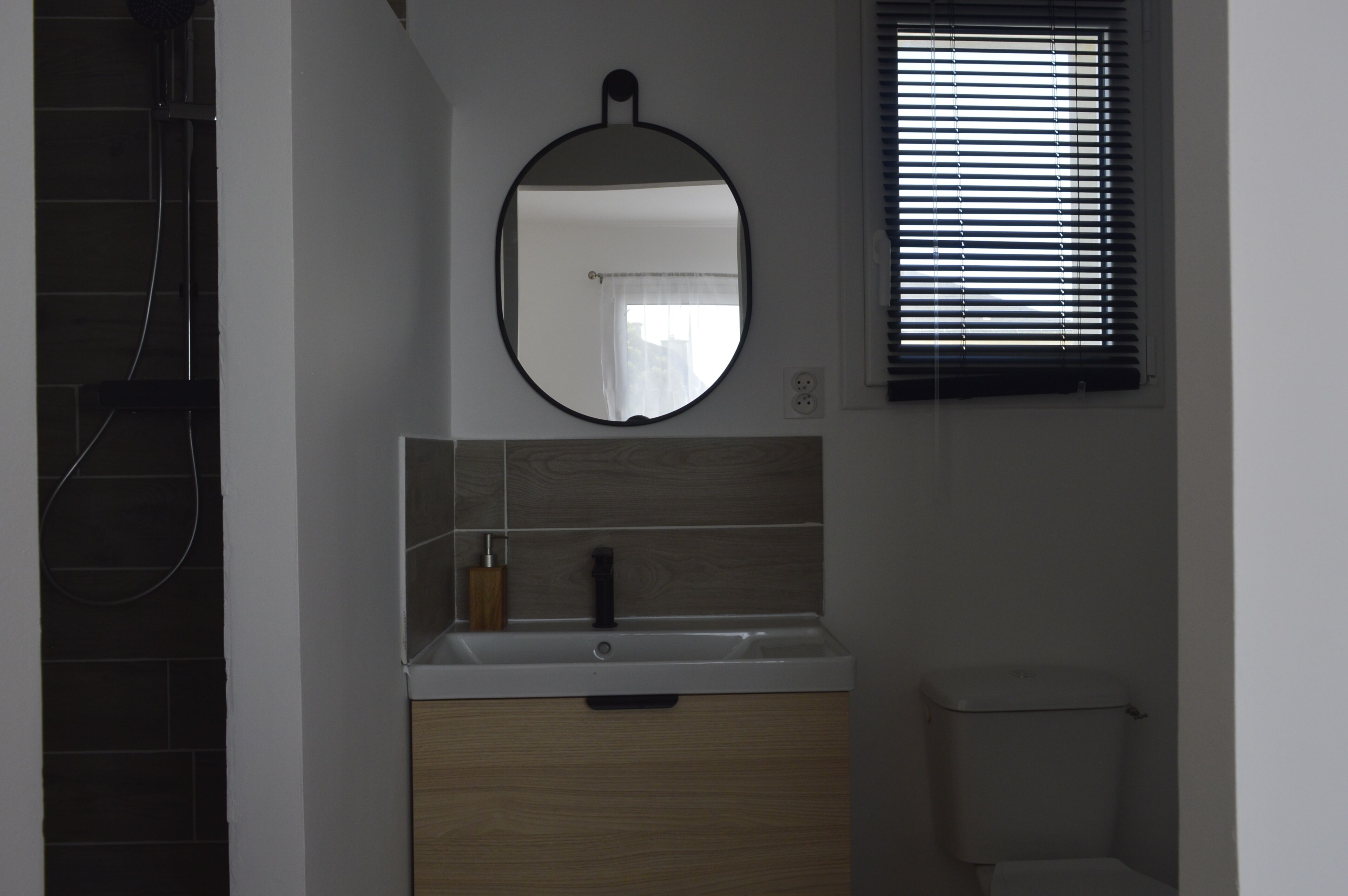 A bathroom with a round mirror, a sink with a wooden cabinet, and a toilet.