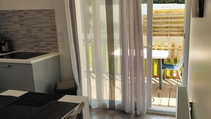 A kitchen with a modern design, a dining area with a table and chairs, and a view of a wooden deck outside. - Résidence des dunes (Landéda)