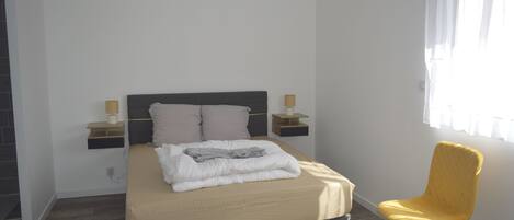 A bedroom with a bed, bedside lamps, a chair, and a window with curtains.