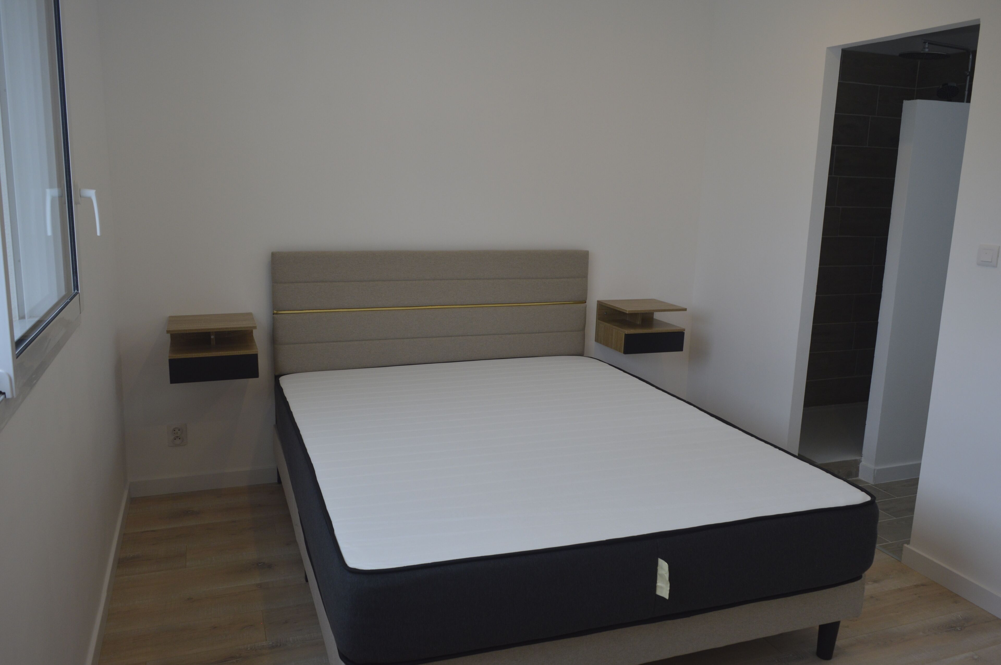 Un lit simple avec une tête de lit, deux tables de chevet et une porte donnant sur un couloir.