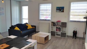 A modern living room with a sofa, coffee table, and bookshelves. - Résidence des dunes (Landéda)