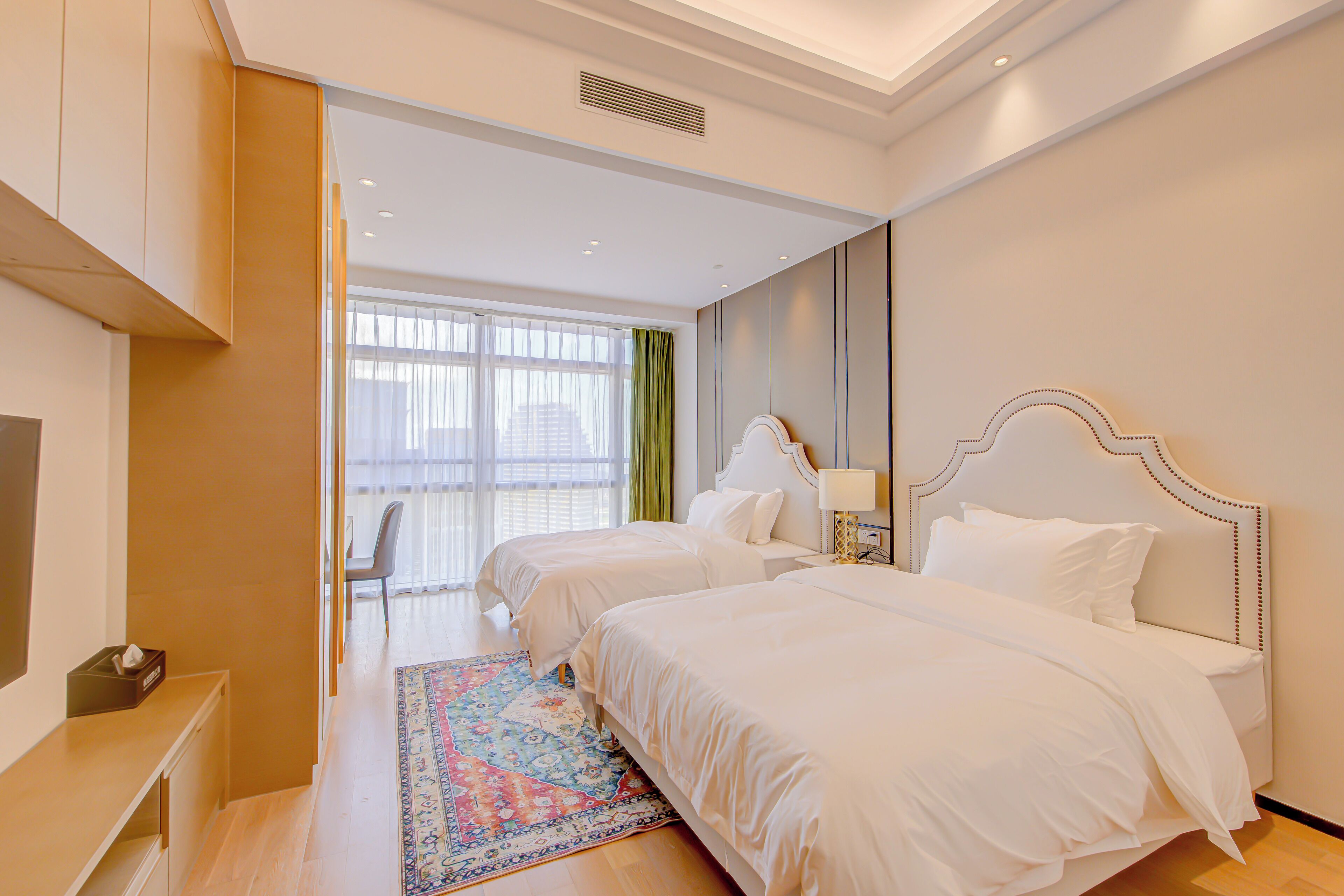 A hotel room with two beds, a desk, and a large window with curtains.