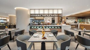 Un restaurant moderne doté d’un bar central, de nombreuses tables et d’un plafond haut avec des luminaires encastrés.