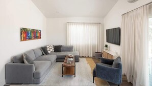 Una sala de estar moderna con un sofá seccional gris, una mesa de centro de madera, un sillón azul y un televisor de pantalla plana montado en la pared.