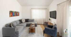 Un salon moderne avec un canapé d’angle gris, une table basse en bois et un fauteuil bleu.