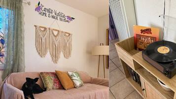Una habitación con sofá, decoración de macramé en la pared, un perro, una lámpara y un tocadiscos.