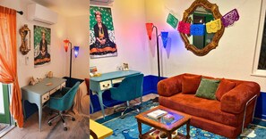 Una habitación con un escritorio, una silla azul, un sofá rojo y una mesa de centro.