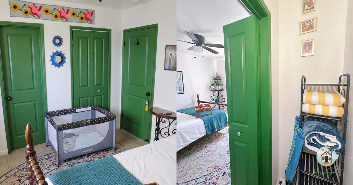 Een kamer met groene deuren, een ledikant, een bed met een blauwe deken, een plafondventilator en een metalen rek met handdoeken.
