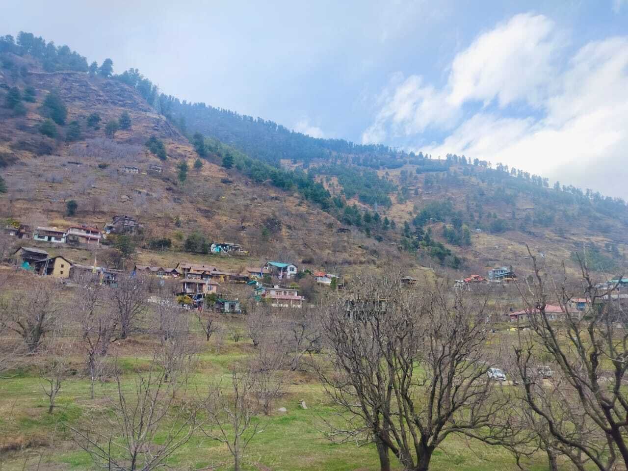A rural village with houses on a hillside, surrounded by trees and open fields.