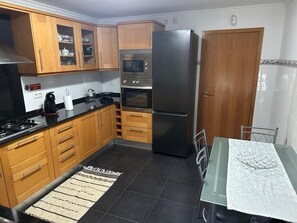 A kitchen with wooden cabinets, a black refrigerator, a stove, and a dining table with chairs.
