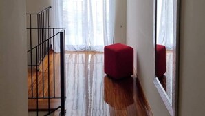 Une pièce dotée d’un plancher en bois, d’un pouf rouge, d’un grand miroir et d’un escalier avec une rampe en métal.