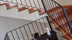 Un escalier avec des marches en bois et des rampes noires, menant à un palier où se trouvent une table en verre et des objets décoratifs.