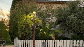 Un muro de piedra con cerca de piquetes blancos, una farola y un cartel.