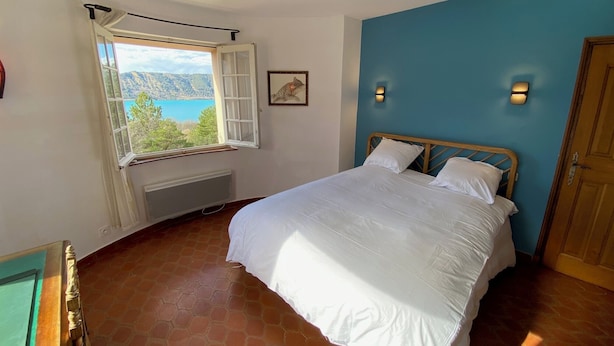 Un dormitorio con cama, ventana con vistas a un lago y pared azul.