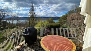 Un patio con una mesa redonda y sillas, una parrilla y vistas a un lago y montañas.
