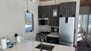 A modern kitchen with dark wood cabinets, stainless steel appliances, a white marble countertop, and a hanging light fixture.