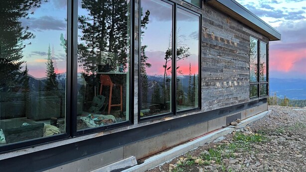 A modern building with large windows reflecting trees and a sunset.