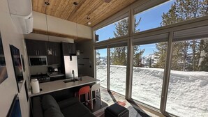 A modern kitchen with a dining area, large windows, and a view of a snowy landscape.