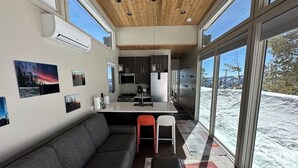 A modern interior with a wooden ceiling, a kitchen area, and large windows offering a snowy view.