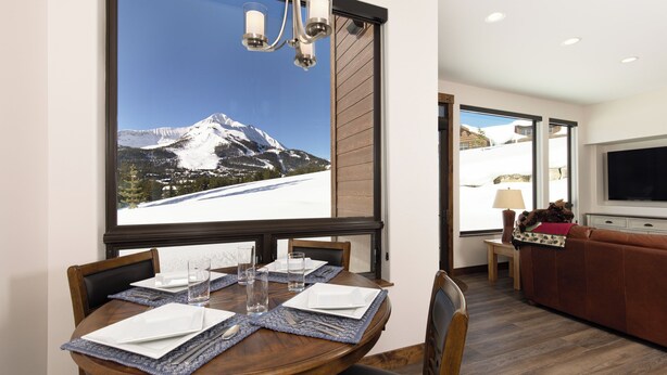 A dining area with a mountain view, a TV, and a sofa in a modern interior. - Silver Aspen | Fire Pit, Hot Tub & Views (Big Sky)