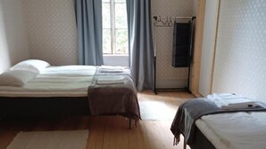 Una habitación con dos camas, una ventana con cortinas, suelo de madera y un perchero.