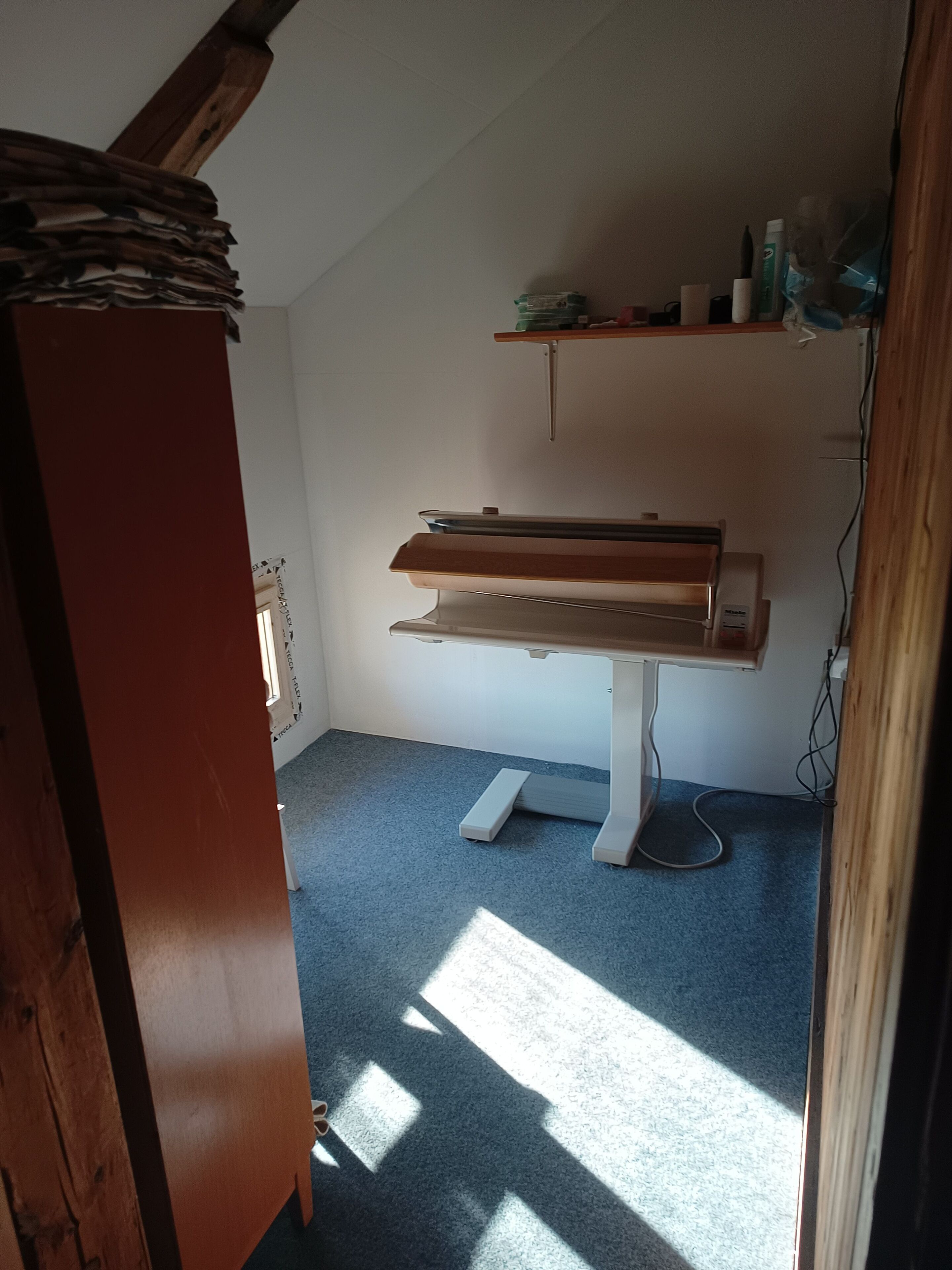 Quarto com escrivaninha de madeira, tapete azul e teto inclinado.
