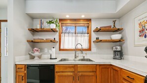 A kitchen with wooden cabinets, a dishwasher, a sink, and a window with curtains. - Old Town Basecamp 6 Blocks to Old Town Square (Fort Collins)