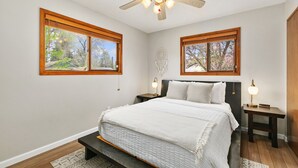 A bedroom with a bed, two nightstands, a ceiling fan, and two windows with wooden frames. - Old Town Basecamp 6 Blocks to Old Town Square (Fort Collins)