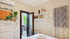 A bedroom with a bed, a dresser, a mirror, a potted plant, a window, and a door leading to an outdoor area. - Regarda -Blue View 3  Apartment with lake view and pool (Bardolino)