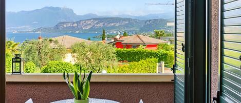 A balcony with a table, chairs, a potted plant, and a view of a lake and mountains.