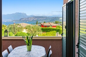 A balcony with a table, chairs, a potted plant, and a view of a lake and mountains.