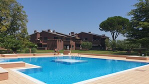 A rectangular swimming pool with a tiled deck, surrounded by a landscaped garden and a multi-story building in the background. - Regarda -Blue View 3  Apartment with lake view and pool (Bardolino)