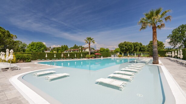A swimming pool with lounge chairs and palm trees.