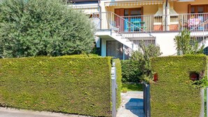 A residential building with a balcony, a gate, and a well-maintained hedge.