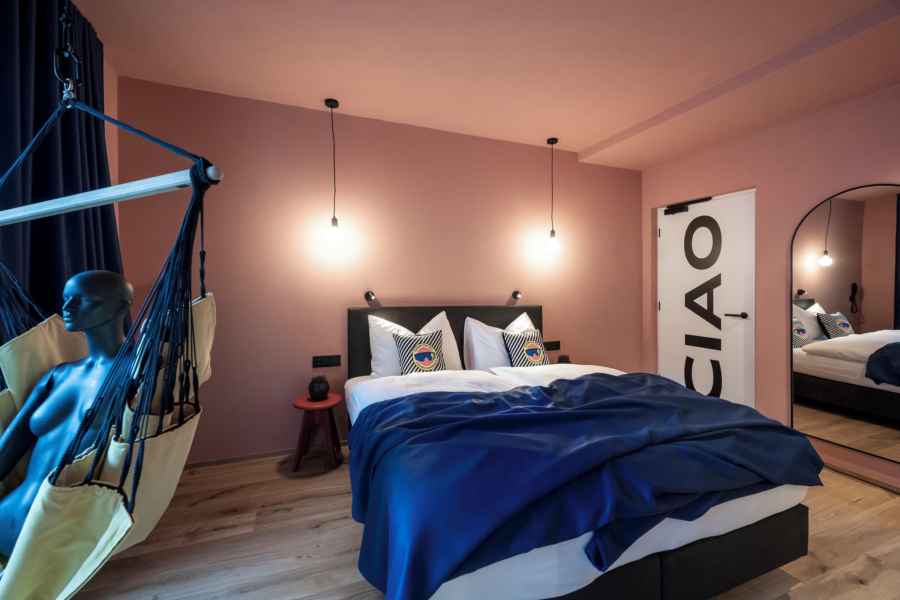 A bedroom with a bed, a hanging chair, a small stool, a mirror, and a door with a sign.