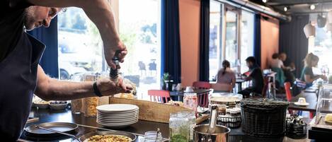Montaje de un bufé de desayuno con diversos alimentos y utensilios.